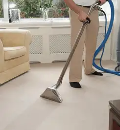 Professional carpet cleaner using a hot-water extraction wand and hose machine in a living room in Fargo, ND.