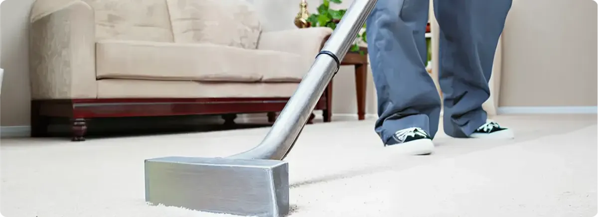 Carpet cleaning technician using a hot-water extraction wand on a light-colored carpet in a living room, Fargo, ND.