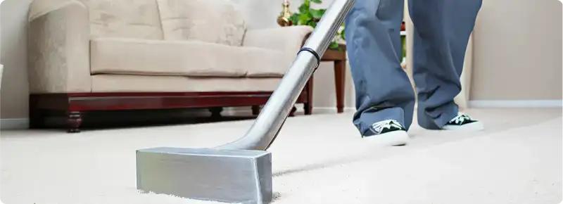 Carpet cleaning technician using a hot-water extraction wand on a light-colored carpet in a living room, Fargo, ND.