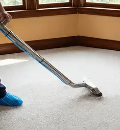 Steam carpet cleaning technician using a hot-water extraction wand on a residential carpet, wearing blue protective shoe covers Fargo, ND.
