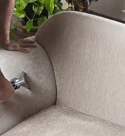 Professional upholstery cleaner deep-cleaning a fabric sofa with a handheld extraction tool and hose Fargo, ND.