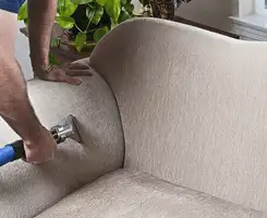 Professional upholstery cleaner deep-cleaning a fabric sofa with a handheld extraction tool and hose in Fargo, ND.
